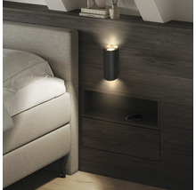 Applique murale moderne à texture striée dans une chambre, diffusant de la lumière vers le haut et le bas au-dessus d'une étagère de lit.