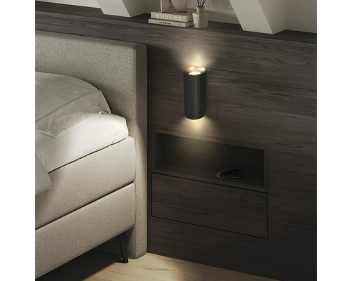 Applique murale moderne à texture striée dans une chambre, diffusant de la lumière vers le haut et le bas au-dessus d'une étagère de lit.