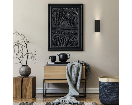Intérieur moderne avec applique noire, tableau abstrait, buffet en bois, plaid gris, vase avec branches et panier tressé.