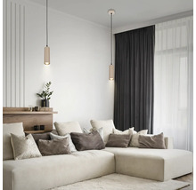 Salon moderne avec deux suspensions cylindriques au-dessus d'un canapé d'angle clair, de nombreux coussins et des rideaux sombres.