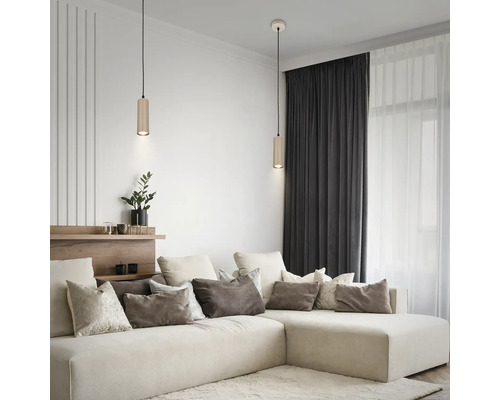 Salon moderne avec deux suspensions cylindriques au-dessus d'un canapé d'angle clair, de nombreux coussins et des rideaux sombres.