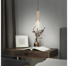 Suspension cylindrique moderne avec surface nervurée au-dessus d'un bureau en bois avec des objets décoratifs.