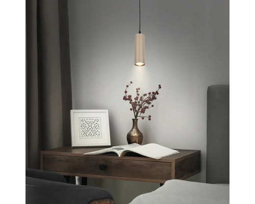 Suspension cylindrique moderne avec surface nervurée au-dessus d'un bureau en bois avec des objets décoratifs.