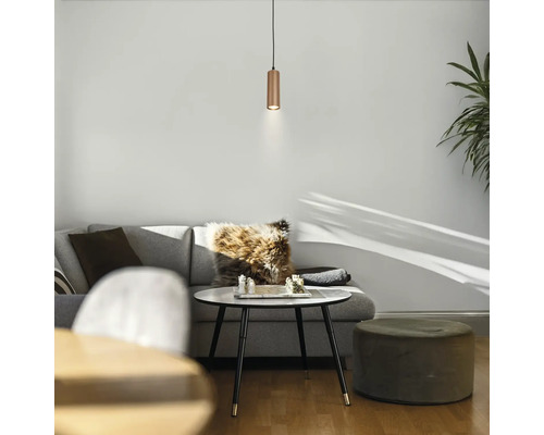 Suspension cylindrique aspect cuivre au-dessus d'une table basse dans un salon clair et moderne avec un canapé gris.