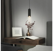Suspension cylindrique noire moderne avec une texture striée au-dessus d'un bureau en bois avec un livre et un vase de baies.