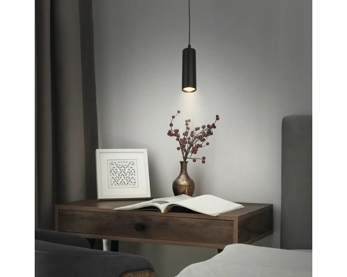 Suspension cylindrique noire moderne avec une texture striée au-dessus d'un bureau en bois avec un livre et un vase de baies.