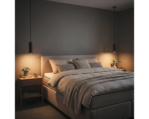 Chambre à coucher moderne avec lit capitonné, coussins gris, deux suspensions cylindriques noires et une table de chevet en bois.
