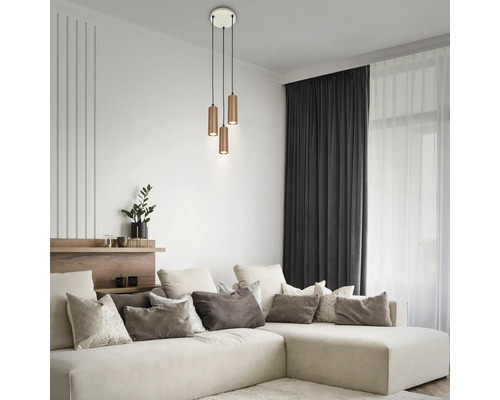 Suspension à trois lampes avec abat-jour cylindriques en métal dans un salon moderne et lumineux avec canapé d'angle et coussins décoratifs.
