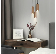 Suspension à trois lampes avec abat-jour cylindriques nervurés au-dessus d'un bureau en bois avec vase et cadre photo dans une pièce moderne.