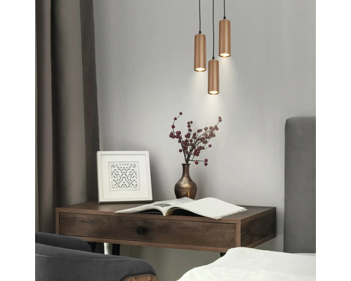 Suspension à trois lampes avec abat-jour cylindriques nervurés au-dessus d'un bureau en bois avec vase et cadre photo dans une pièce moderne.