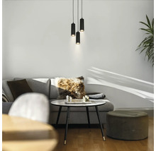 Trois suspensions cylindriques noires au-dessus d'un coin salon moderne avec un canapé gris, une table basse ronde et un pouf.