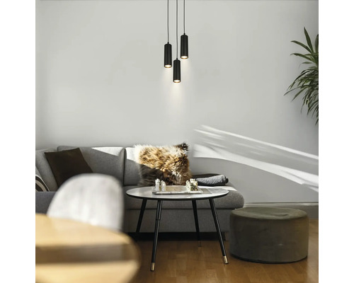 Trois suspensions cylindriques noires au-dessus d'un coin salon moderne avec un canapé gris, une table basse ronde et un pouf.