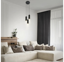 Salon moderne avec une suspension cylindrique noire à trois lampes au-dessus d'un grand canapé d'angle beige avec divers coussins.