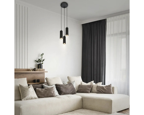 Salon moderne avec une suspension cylindrique noire à trois lampes au-dessus d'un grand canapé d'angle beige avec divers coussins.