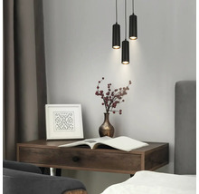 Scène moderne avec trois suspensions cylindriques noires au-dessus d'un bureau en bois sombre avec vase, cadre photo et livre ouvert.