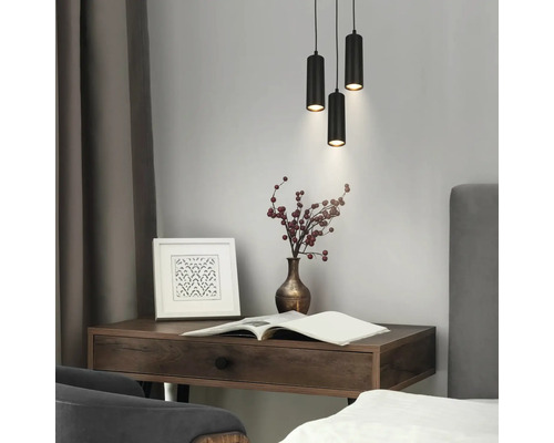 Scène moderne avec trois suspensions cylindriques noires au-dessus d'un bureau en bois sombre avec vase, cadre photo et livre ouvert.