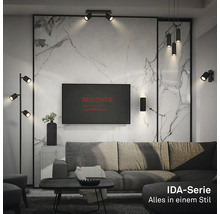 Salon moderne avec luminaires noirs de la série Briloner IDA, dont lampadaire, suspensions et appliques devant un mur en marbre.