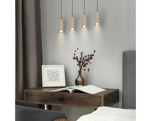 Suspension à quatre lampes avec abat-jour cylindriques aspect bois au-dessus d'un bureau en bois dans une pièce moderne.