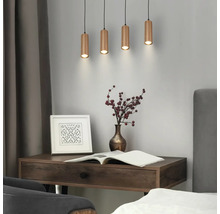 Quatre suspensions cylindriques avec une finition nervurée au-dessus d'un bureau en bois avec un livre, un vase et un cadre dans une pièce moderne.