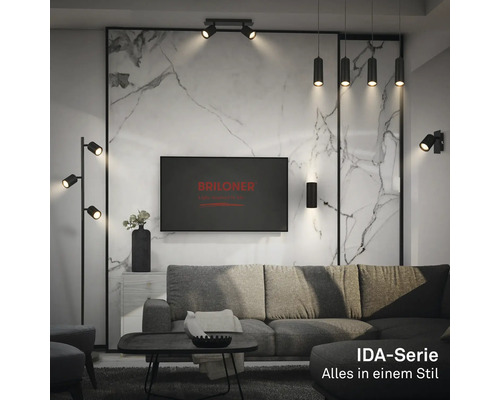 Salon moderne avec luminaires noirs de la série IDA : lampadaire, suspensions et spots. Mur aspect marbre, canapé gris. Briloner Logo.