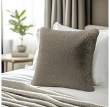 Quadratisches Dekokissen aus Kunstfell auf einem Bett mit Strickdecke in einem hellen Schlafzimmer.