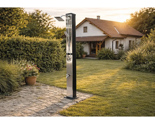 Moderne Solardusche aus Edelstahl im Garten mit Regenduschkopf, Handbrause und Fußbrause auf einem gepflasterten Weg neben einer Rasenfläche.