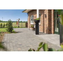 Terrasse spacieuse avec des pavés en béton devant une maison en briques, comprenant un banc de jardin et un bac à fleurs décoratif.
