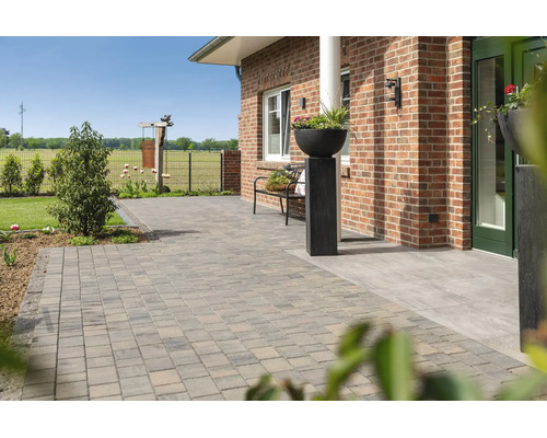 Terrasse spacieuse avec des pavés en béton devant une maison en briques, comprenant un banc de jardin et un bac à fleurs décoratif.