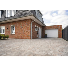 Extérieur de maison en briques avec porte de garage blanche et grande allée pavée de pierres rectangulaires.