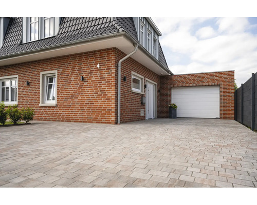 Extérieur de maison en briques avec porte de garage blanche et grande allée pavée de pierres rectangulaires.