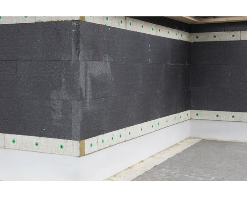 Mur extérieur avec panneaux isolants sombres et bandes de finition claires, fixés avec des chevilles pour isolant sur un angle de bâtiment.