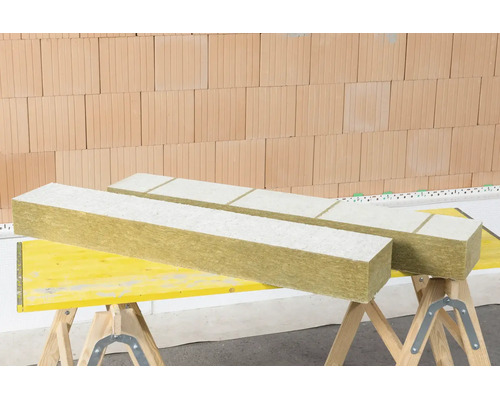 Panneaux isolants en laine minérale avec revêtement blanc sur tréteaux devant un mur en briques.