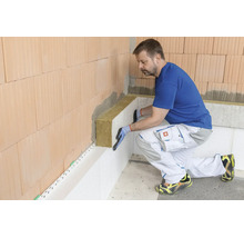 Un artisan pose des panneaux isolants en laine minérale sur un mur en briques pour une isolation thermique intérieure professionnelle.