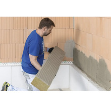 Artisan appliquant un panneau isolant en laine de roche avec du mortier-colle sur un mur en briques.