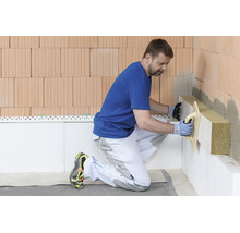 Un artisan installe des panneaux isolants en laine minérale sur un mur en briques.