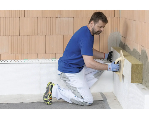 Un artisan installe des panneaux isolants en laine minérale sur un mur en briques.