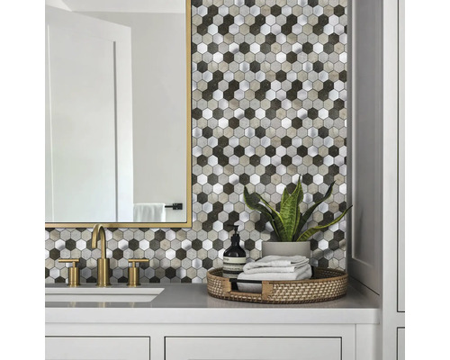 Badezimmer-Szene mit hexagonalem Mosaik-Fliesenspiegel in Stein- und Metalloptik, kombiniert mit goldfarbener Armatur und hellem Waschtisch.