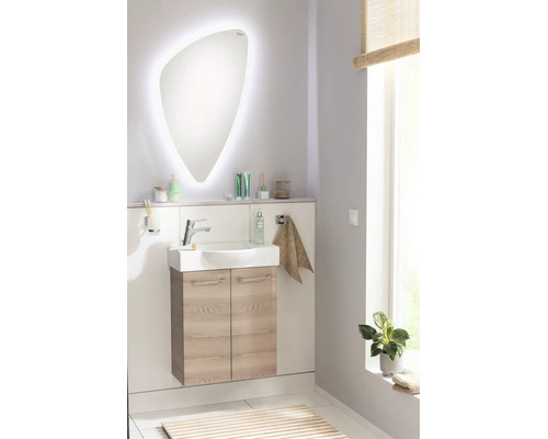 Modernes Badezimmer-Set bestehend aus einem organisch geformten LED-Spiegel, Keramikwaschtisch und hängendem Unterschrank in heller Eiche-Optik.