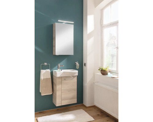 Salle de bain moderne avec meuble sous-lavabo en bois clair, lavabo en céramique blanche, armoire de toilette avec éclairage et porte-serviettes.
