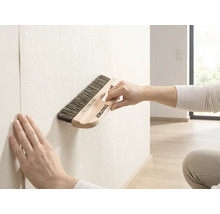 Brosse à tapisser Rautner lors du lissage du papier peint sur un mur dans une pièce lumineuse.