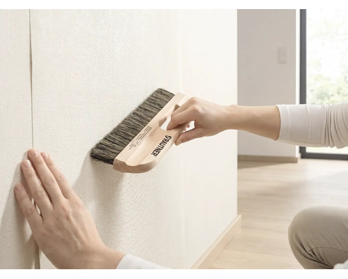 Brosse à tapisser Rautner lors du lissage du papier peint sur un mur dans une pièce lumineuse.