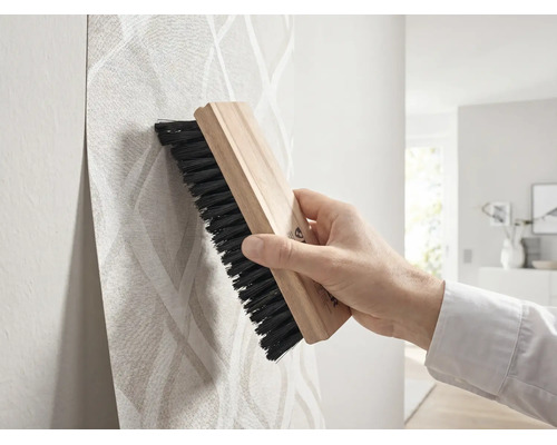 Main lissant du papier peint à motifs avec une brosse à tapisser en bois.