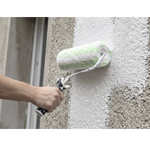 Une main peint une façade à structure grossière à l'aide d'un rouleau à façade.