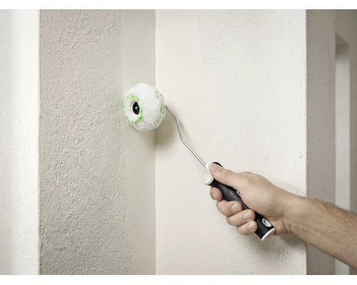 Un petit rouleau d'angle rond est utilisé pour peindre le coin intérieur d'un mur blanc texturé.