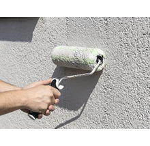 Application de peinture avec un rouleau sur une façade texturée.
