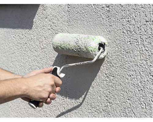 Application de peinture avec un rouleau sur une façade texturée.