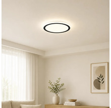 Moderne runde LED-Deckenleuchte mit schwarzem Rand in einem hellen, minimalistischen Wohnzimmer mit weißen Wänden und hellen Möbeln.
