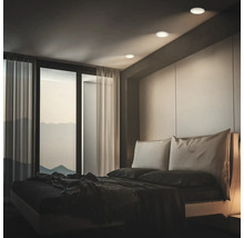 Chambre moderne avec des spots encastrés au plafond diffusant une lumière douce sur le lit avec vue sur les montagnes.