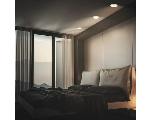 Chambre moderne avec des spots encastrés au plafond diffusant une lumière douce sur le lit avec vue sur les montagnes.
