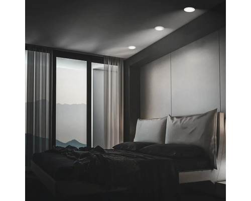 Chambre moderne avec spots encastrés au plafond, baies vitrées et vue sur les montagnes au crépuscule.